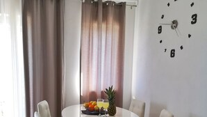 Ein Essbereich mit einem runden Tisch, vier Stühlen, einer Wanduhr und einem Fenster mit Vorhängen.