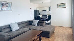 A modern living room with a grey sectional sofa, a wooden coffee table, and a dining area with a black table and chairs. - Magdales - Comfort Three Bedroom Apartment (Omis)