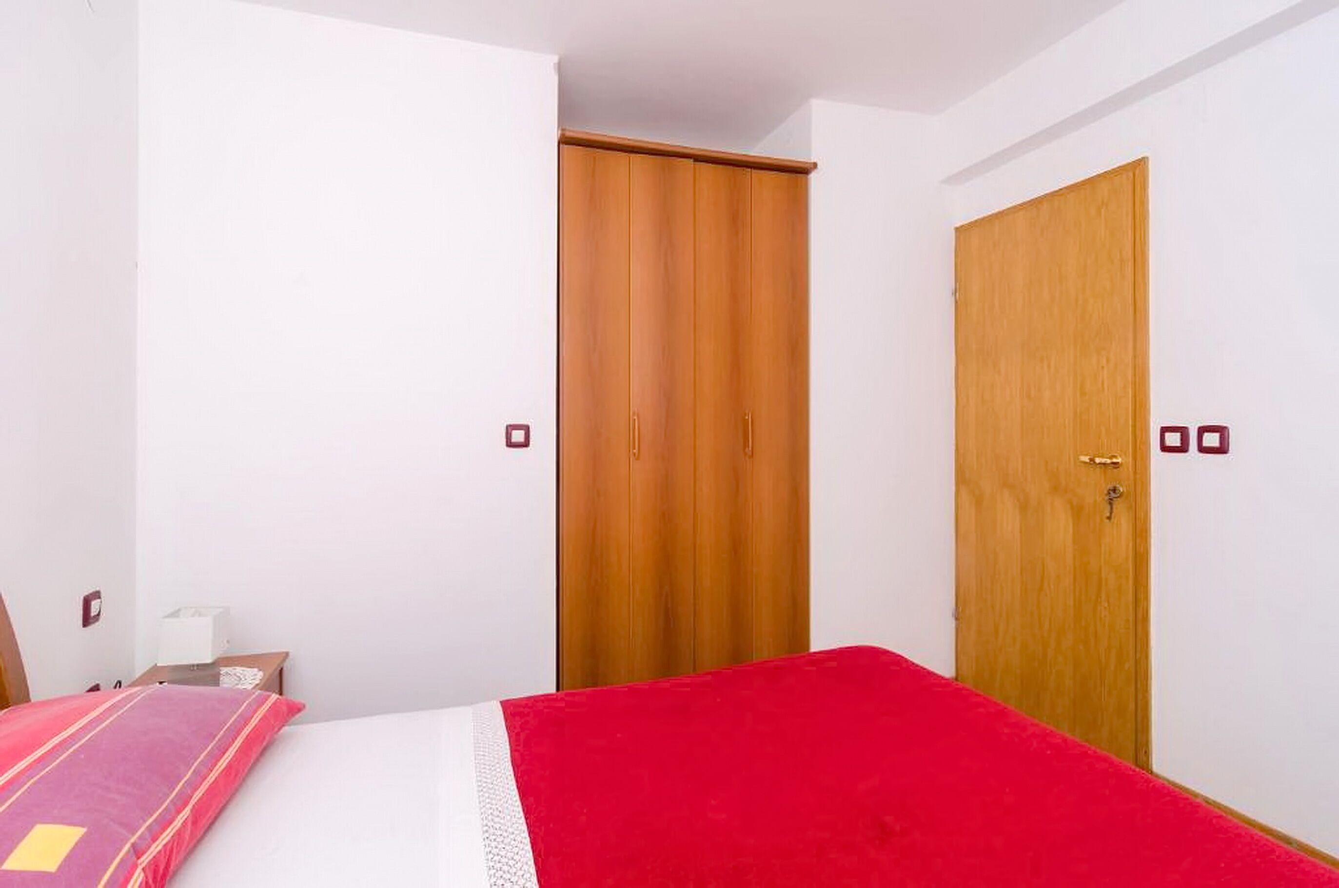 Een slaapkamer met een bed, een houten garderobe en een deur.