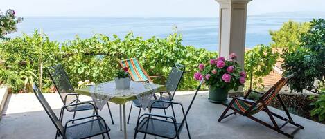 A covered patio with a table and chairs, a hammock, and potted plants.