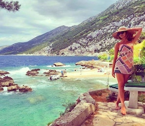 A coastal scene with a rocky beach, clear blue water, and a mountainous backdrop.