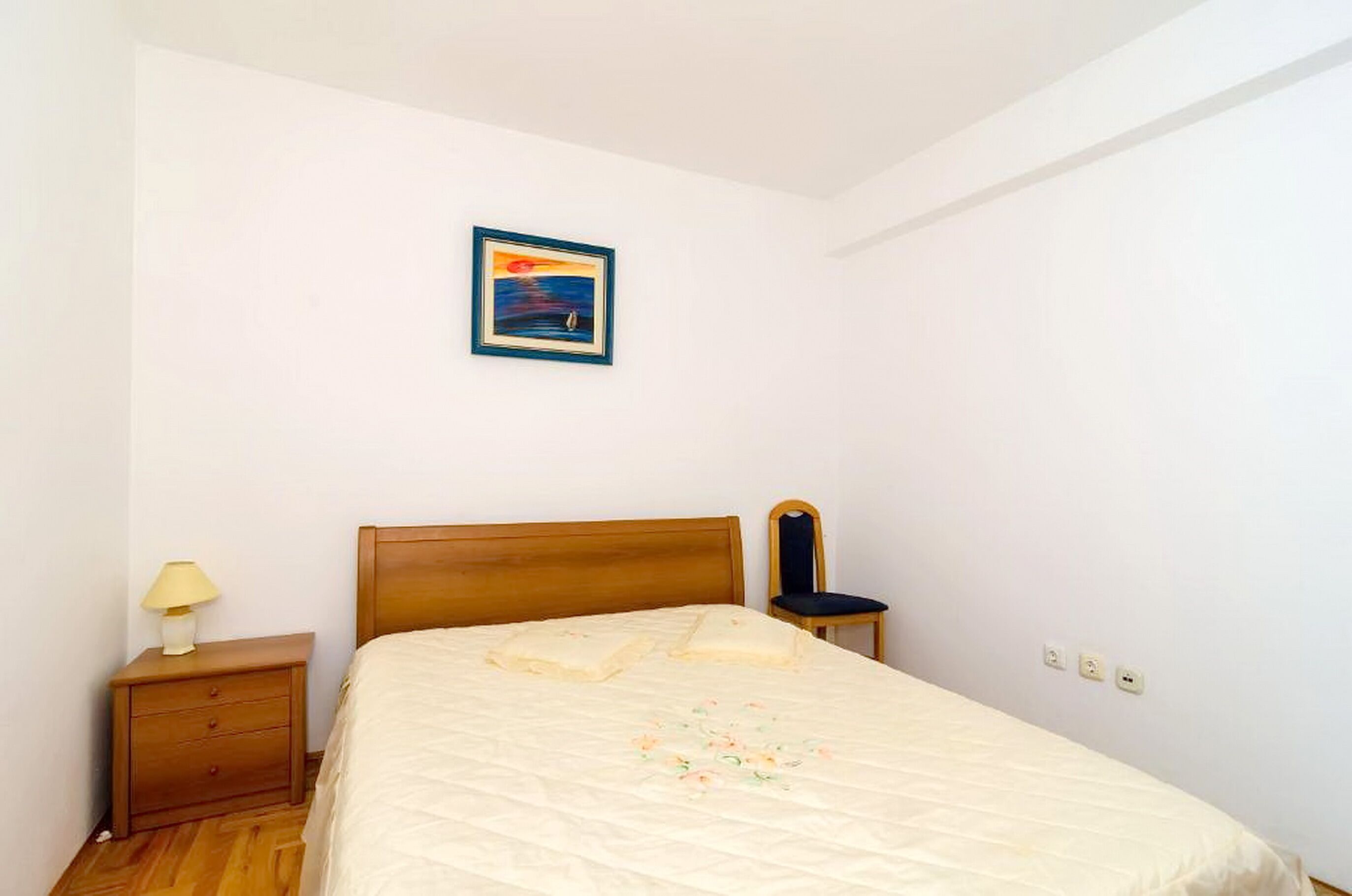 Ein Schlafzimmer mit einem hölzernen Bett, einem Nachttisch mit Lampe, einem Sessel und einem gerahmten Bild an der Wand.
