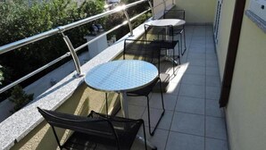 Un balcon avec une table ronde et deux chaises, une rambarde en métal et une vue sur un immeuble et de la verdure.