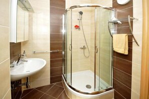 Bathroom features a glass-enclosed shower, handheld showerhead, and wall-mounted faucet.