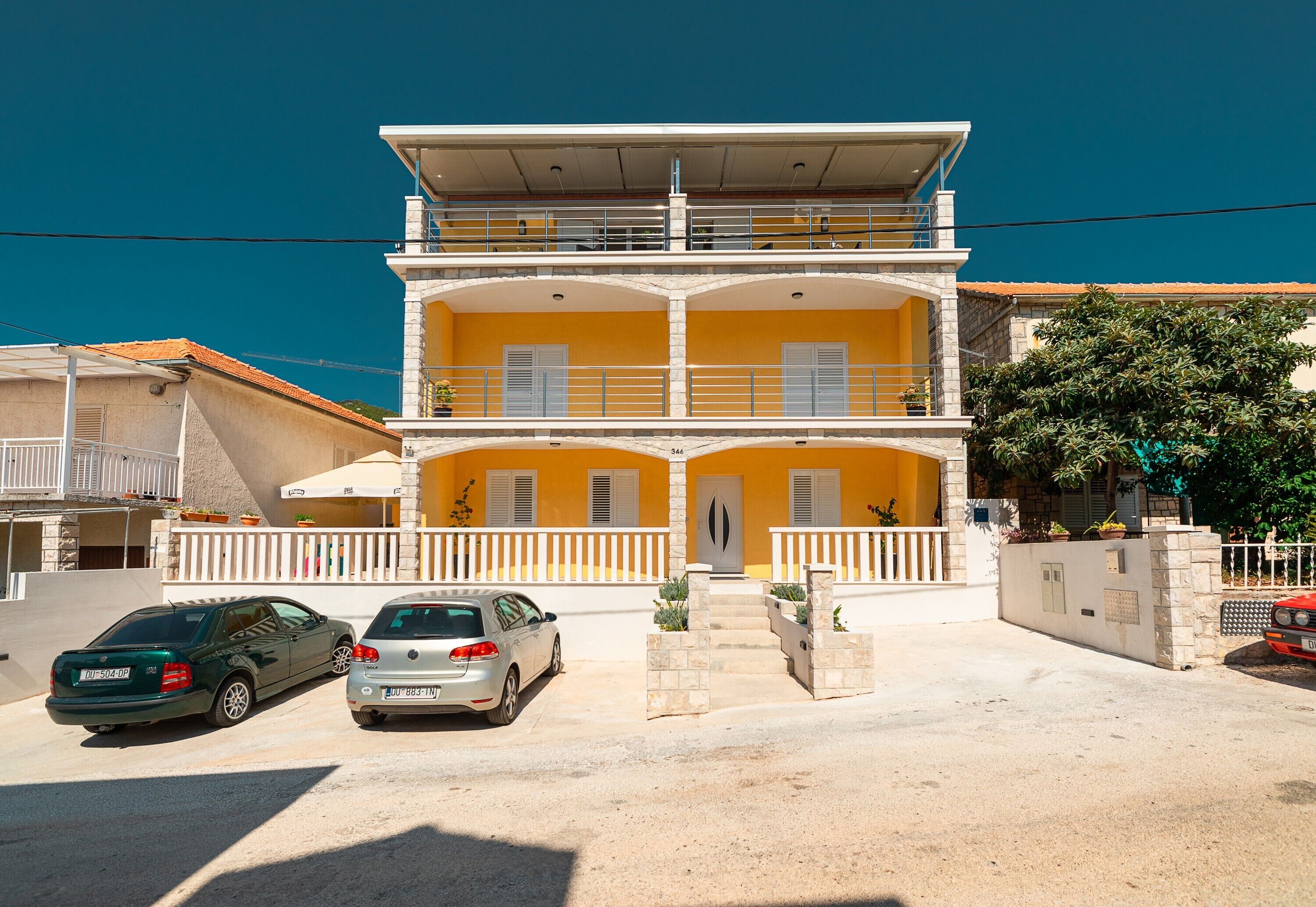 A two-story building with a balcony, a car parked in front, and a clear blue sky.