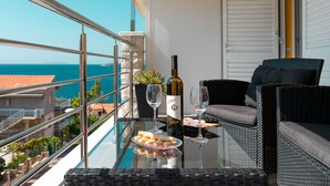 Een balkon met een glazen tafel, rieten meubilair, een fles wijn en een schaal met hapjes.