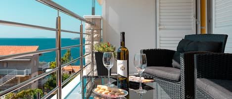 A balcony with a glass table, a bottle of wine, two wine glasses, and a wicker chair.
