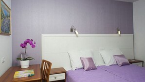Ein Schlafzimmer mit Bett, Nachttisch, Schreibtisch mit Stuhl, einer Topfpflanze und einem Gemälde an der Wand.