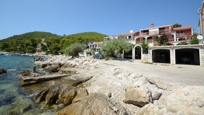 A coastal property with a rocky shoreline, a clear view of the sea, and a hillside in the background.