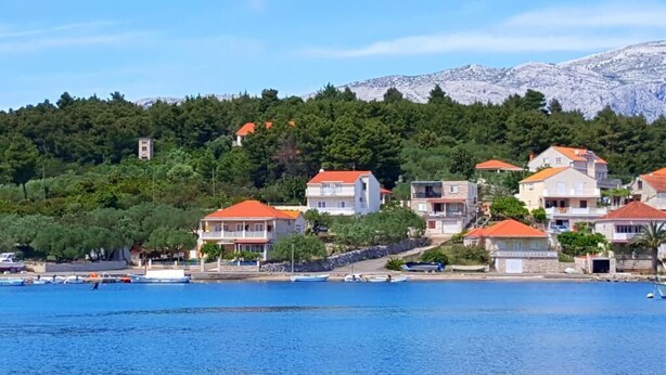 A coastal village with houses on a hillside, a clear blue sea, and boats docked along the shore. - Apartments Radojković Lumbarda -One Bedroom Apartment with Terrace and Partial Sea View(A1) (Lumbarda)