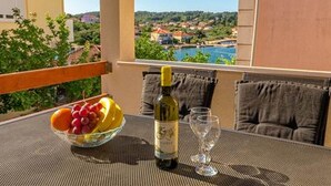 A balcony with a table set for two, featuring a bowl of fruit, a bottle of wine, and two glasses. - Apartments Radojković Lumbarda -One Bedroom Apartment with Terrace and Partial Sea View(A1) (Lumbarda)
