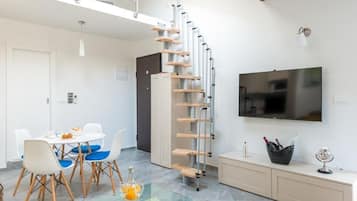 A modern living room with a spiral staircase, a dining area with a glass table, and a flat-screen TV mounted on the wall.
