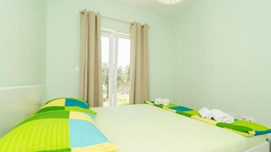 A room with a bed, a window with curtains, and a view of greenery outside.