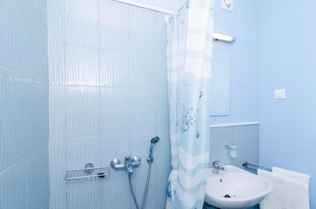 Een badkamer met lichtblauwe tegels, een douche met transparant gordijn, een wastafel en een spiegel.