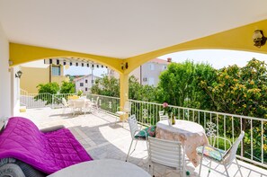 Un balcon aux murs jaunes, avec des balustrades blanches et du mobilier d’extérieur comprenant un canapé violet et une table avec des chaises.