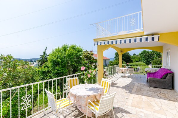Un balcon avec une table et des chaises, un canapé violet et une vue sur la verdure et les collines.