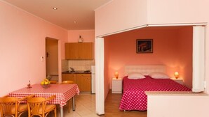 Una habitación compacta con kitchenette, un comedor con una mesa a cuadros y una cama con colcha de lunares.