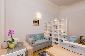 Una sala de estar moderna con un sofá gris, una mesa de comedor con un jarrón de flores y un estante blanco.