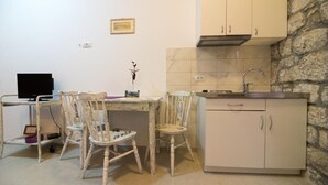 Una cuina compacta amb armaris blancs, una paret de pedra i una zona de menjador amb dues cadires i una taula.