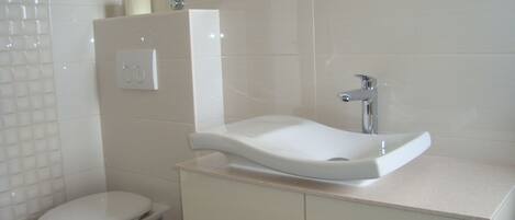 A bathroom with a white toilet, a sink with a mirror above it, and a shower area.