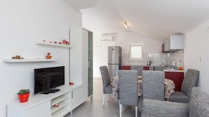 A compact living space with a dining area, kitchenette, and a TV on a white cabinet. - Apartments Memunić - One Bedroom Apartment with Balcony and Sea View (Ston)
