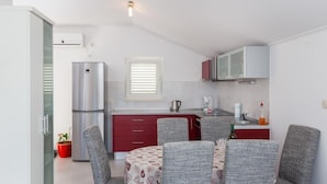 A compact kitchen with a refrigerator, a coffee maker, and a microwave. There is a dining area with a table and four chairs. - Apartments Memunić - One Bedroom Apartment with Balcony and Sea View (Ston)