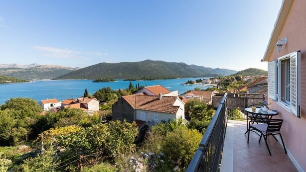 A balcony with a table and chairs overlooking a lake and mountains. - Apartments Memunić - One Bedroom Apartment with Balcony and Sea View (Ston)