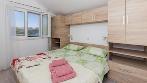 A bedroom with a bed, a window with curtains, and wooden cabinets. - Apartments Memunić - One Bedroom Apartment with Balcony and Sea View (Ston)
