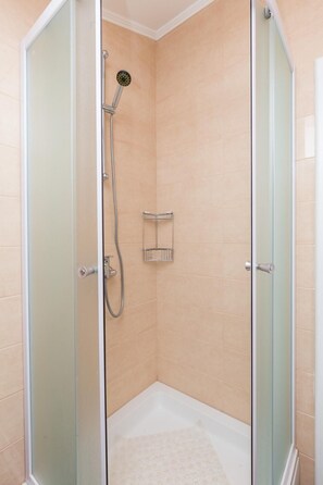 Une cabine de douche fermée par des parois en verre, dotée d’un pommeau de douche à main et d’une petite étagère.