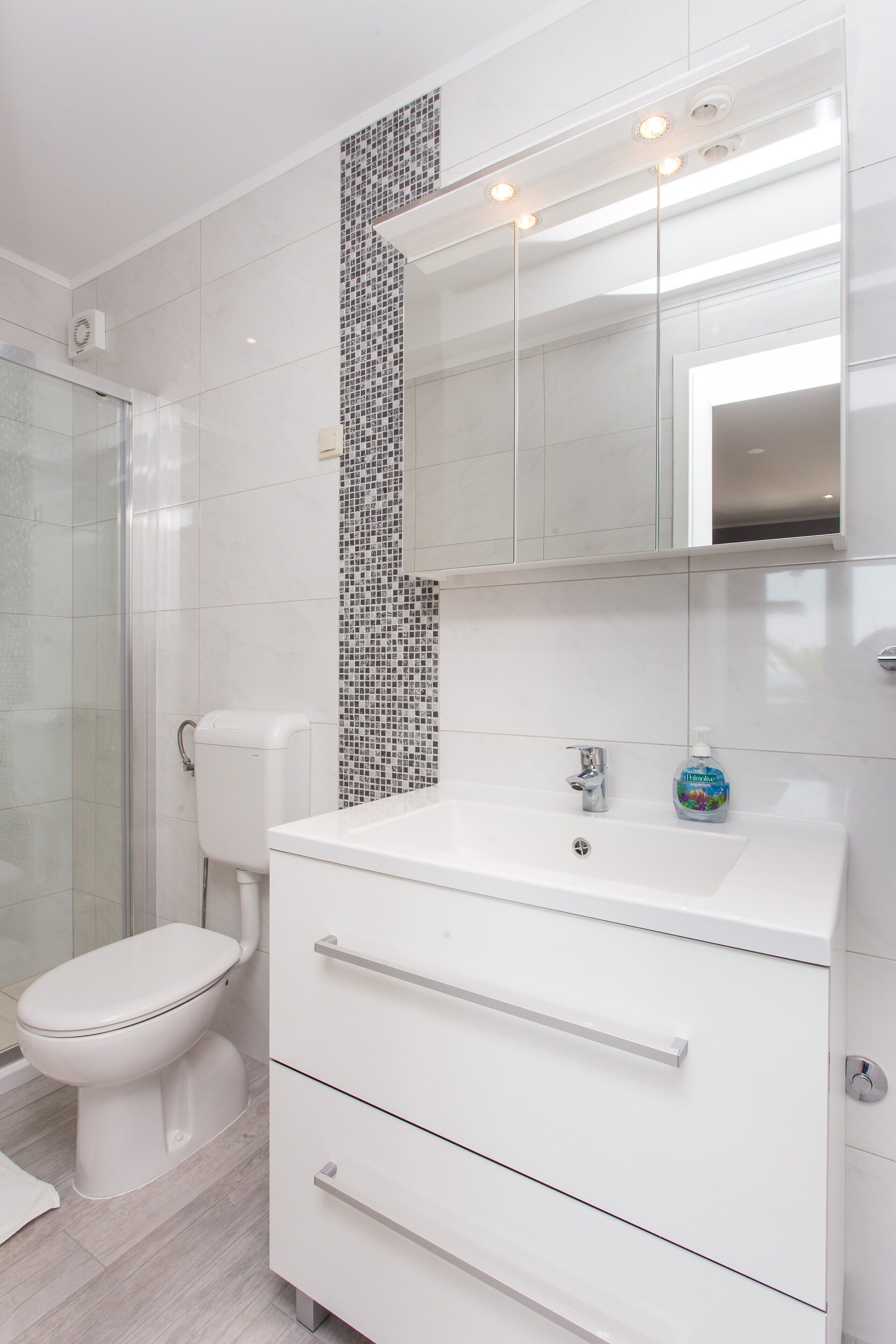 Et moderne badeværelse med toilet, vask med spejl over, og et bruseområde.