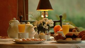 Una mesa de desayuno con una jarra, tazas, un florero y una variedad de pasteles y frutas.