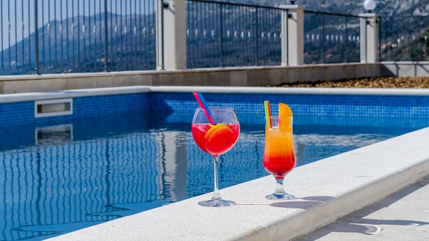 A swimming pool with two drinks on the edge.