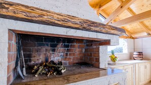 A stone fireplace with logs, wooden beams, and a window overlooking a mountain.