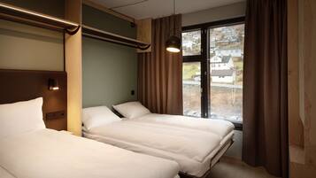 A hotel room with two beds, a window with curtains, and a view of houses outside.
