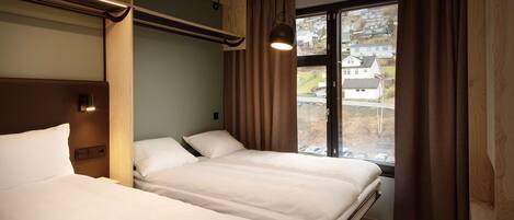A hotel room with two beds, a window with curtains, and a view of houses outside.