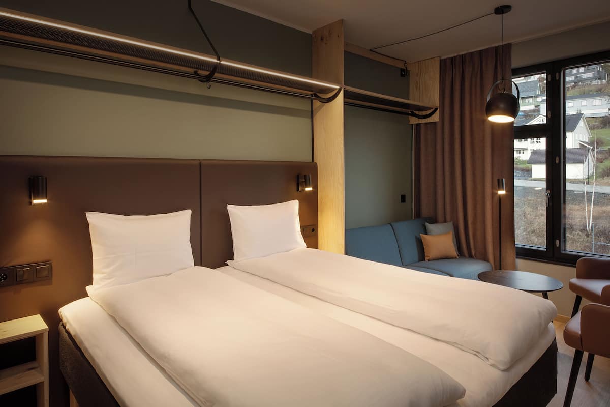 A hotel room with a large bed, a sofa, a small table, and a view of the outside.