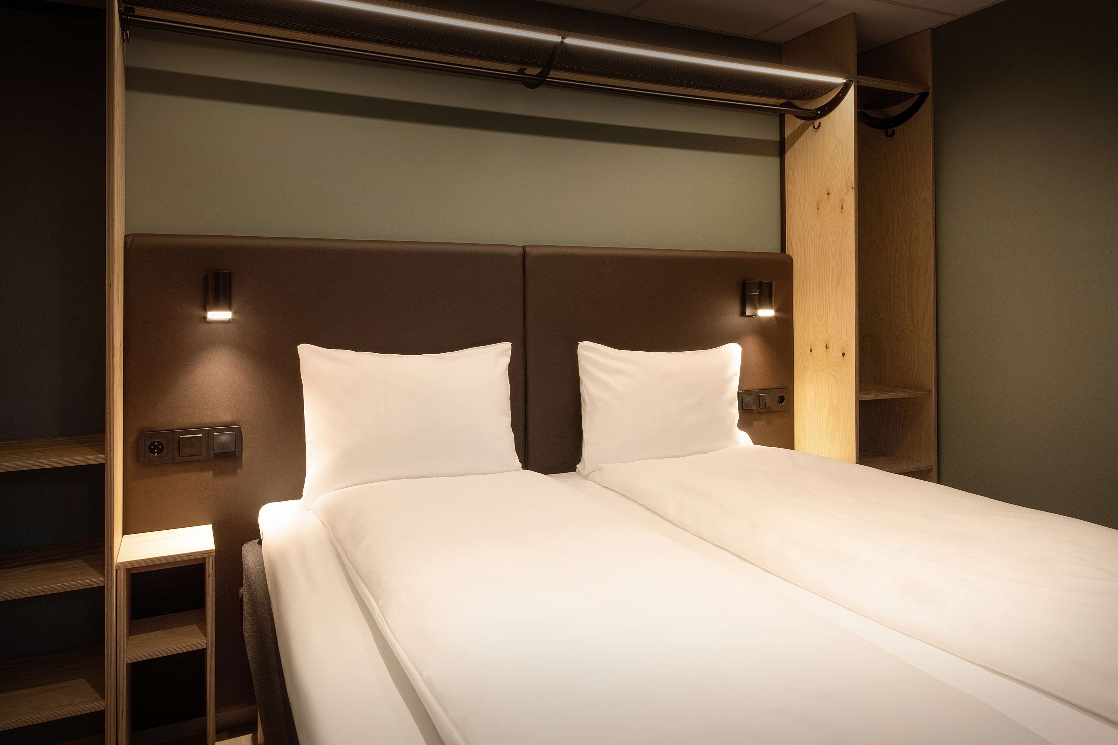A neatly made bed with a headboard, bedside tables, and wall-mounted lighting.