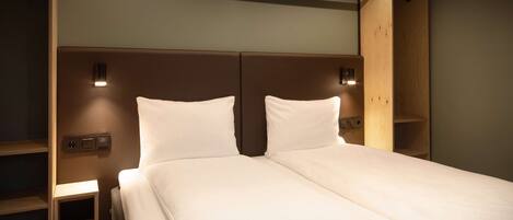 A neatly made bed with a headboard, bedside tables, and wall-mounted lighting.