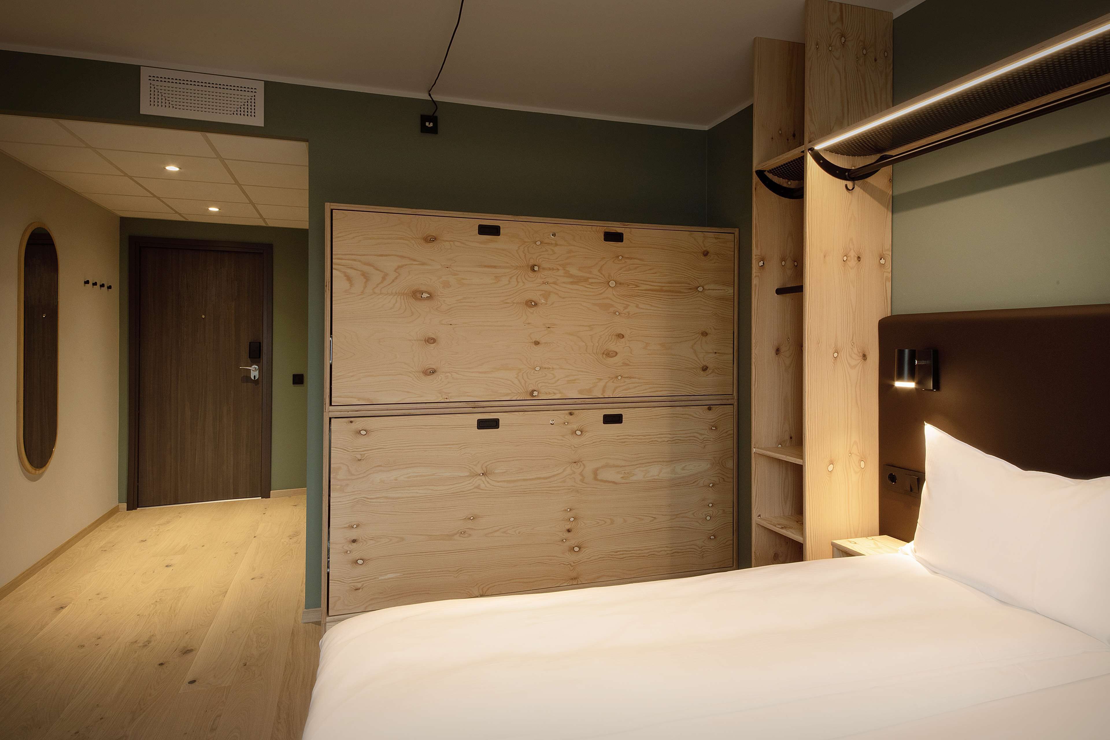 Una habitación de hotel con un armario de madera, una cama con ropa blanca y una mesita de noche de madera.