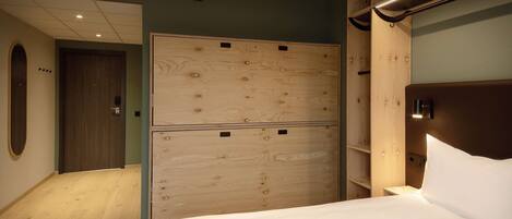 A hotel room with a wooden wardrobe, a bed with white linens, and a wooden nightstand.