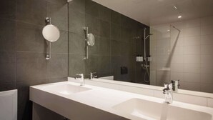 A modern bathroom with two sinks, a large mirror, and a shower.