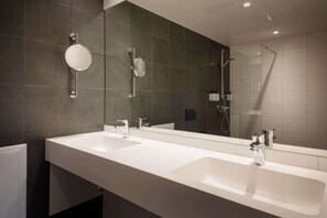 A modern bathroom with two sinks, a large mirror, and a shower.