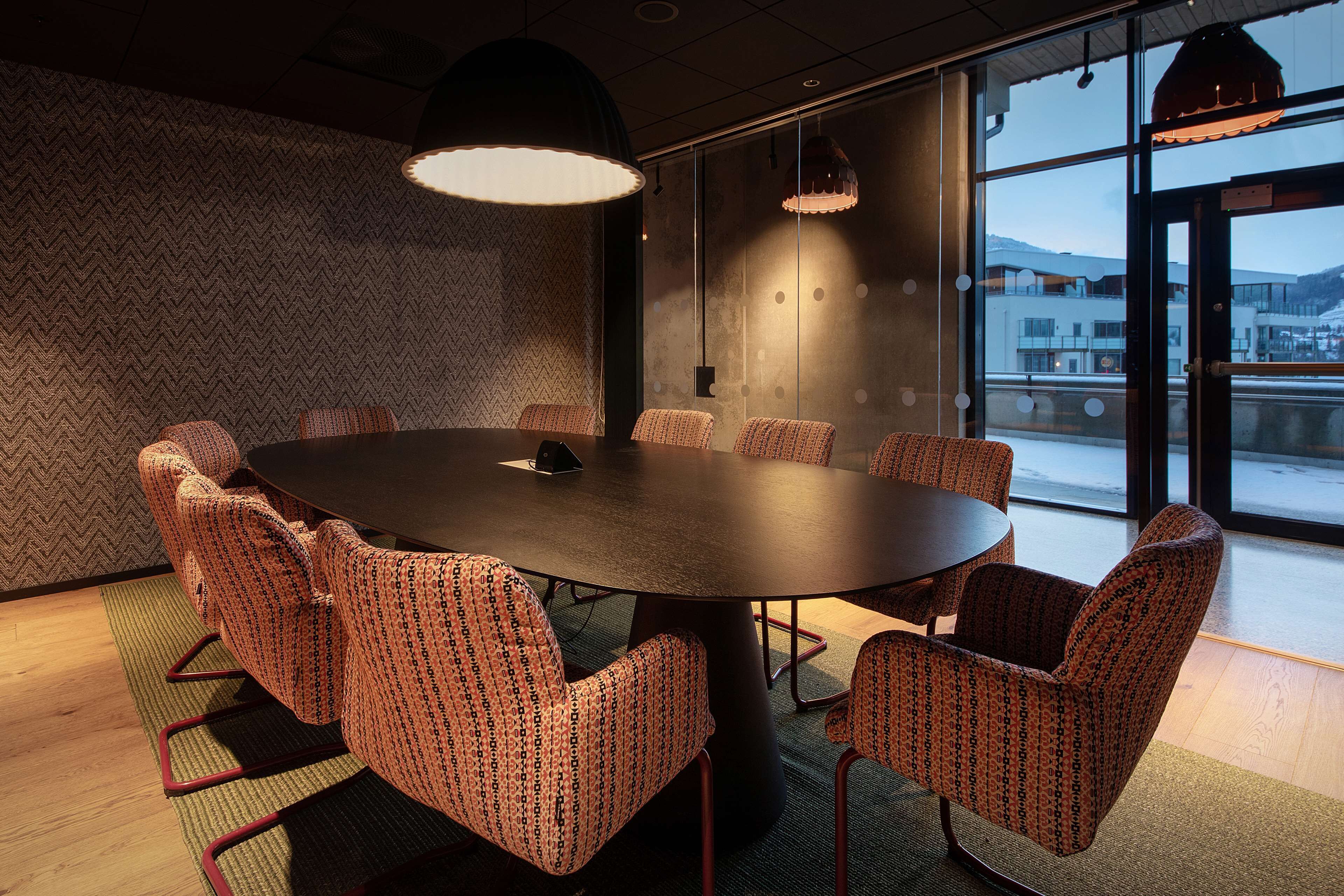 Un salón de conferencias con una mesa redonda, sillas estampadas e iluminación colgante.