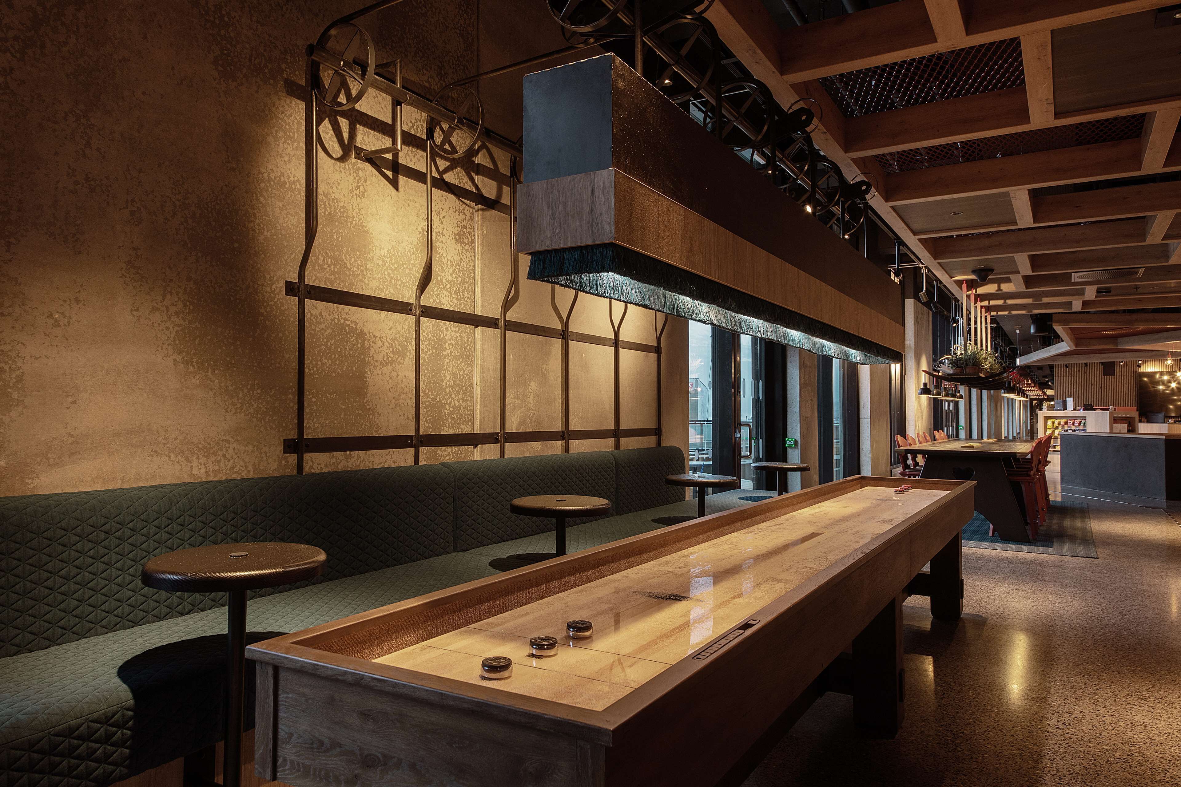 A bar area with a long wooden table, cushioned seating, and a high ceiling with exposed beams.