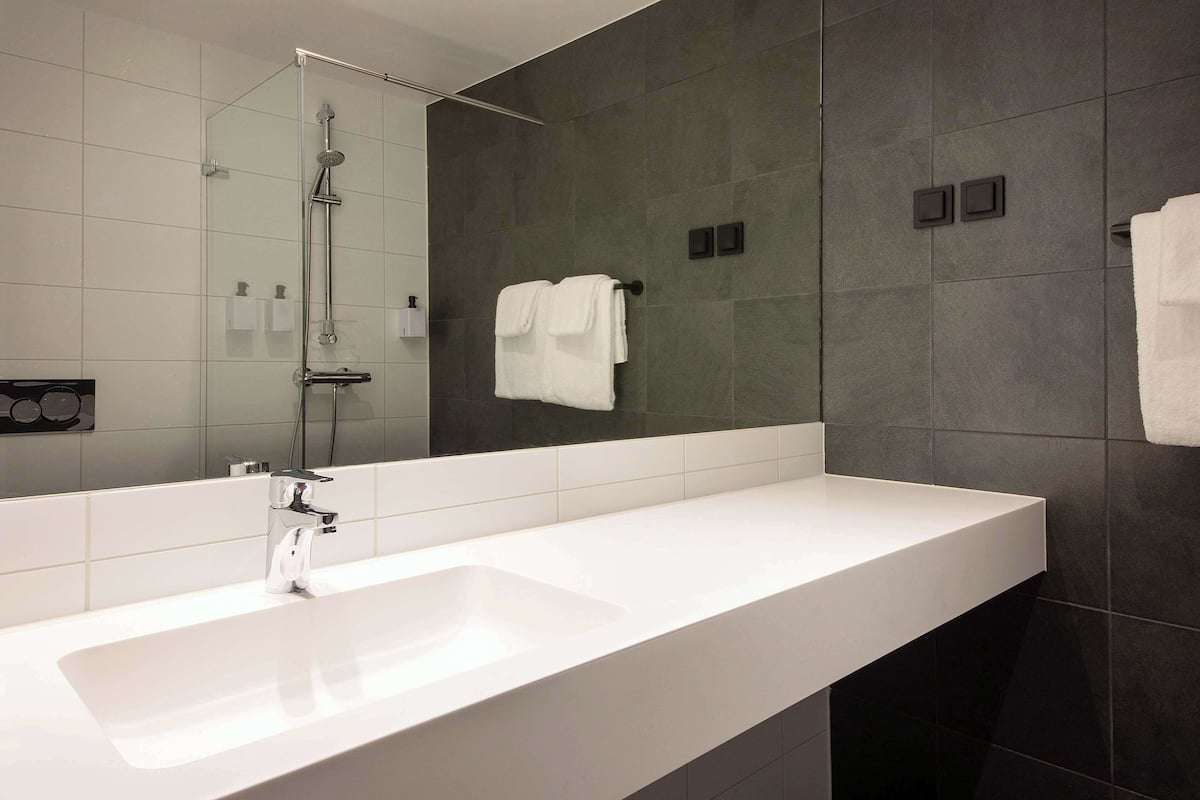 A modern bathroom with a white sink, a glass-enclosed shower, and dark tiled walls.