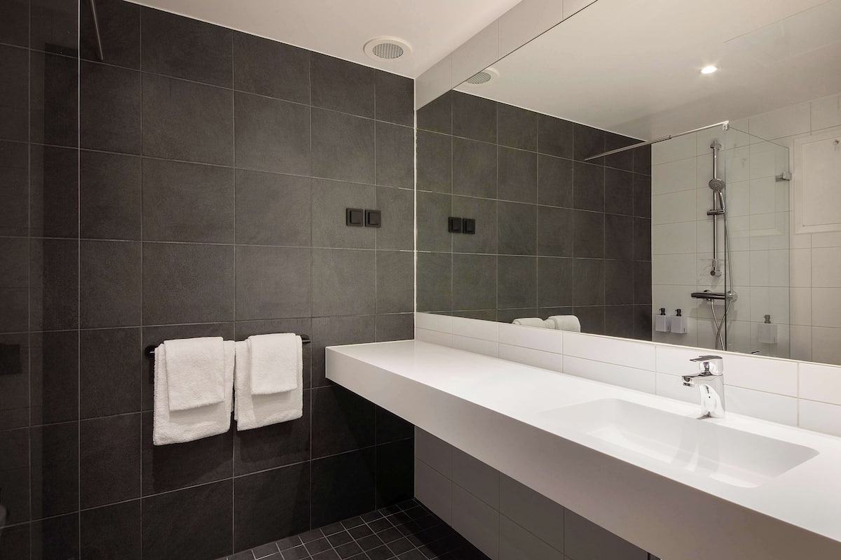 A modern bathroom with dark tiles, a white sink, and a glass shower enclosure.