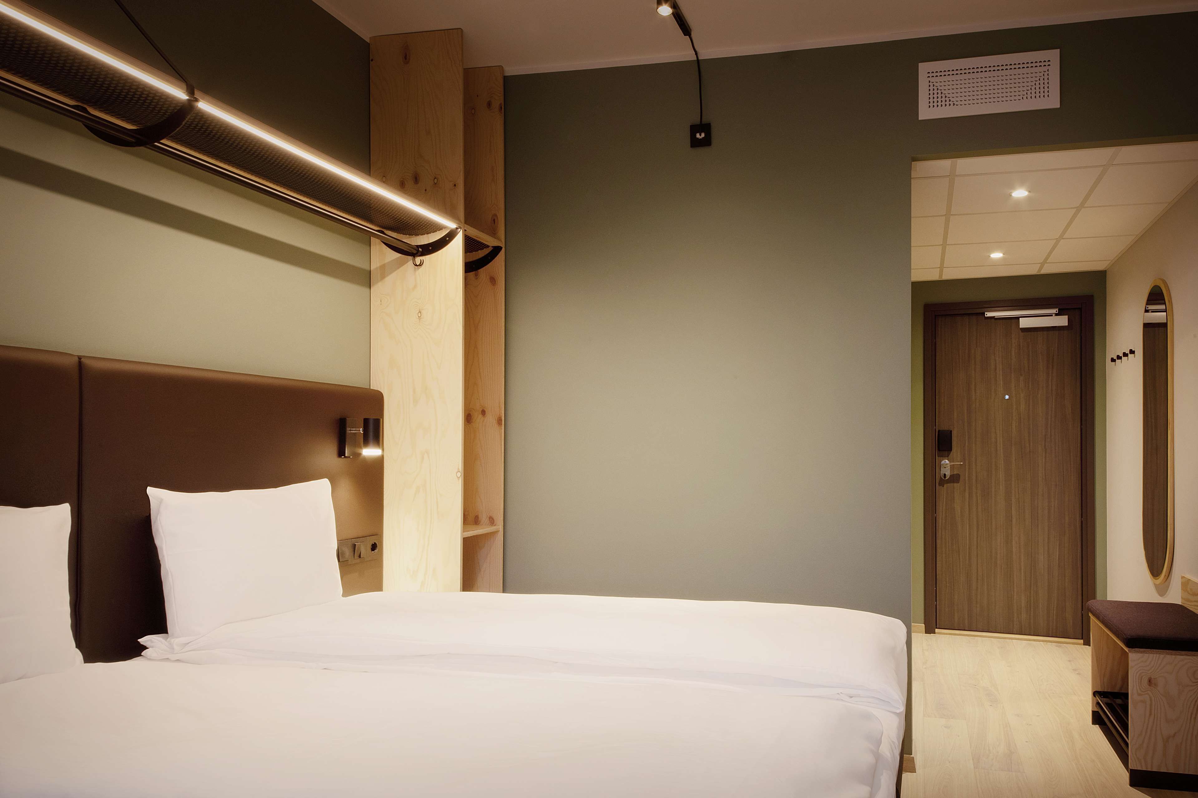 Una habitación de hotel con una cama grande, cabecera de madera y una mesita de noche pequeña.