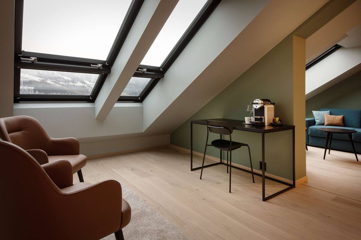 A modern loft bedroom with skylights, a sofa, a small table, and a chair.