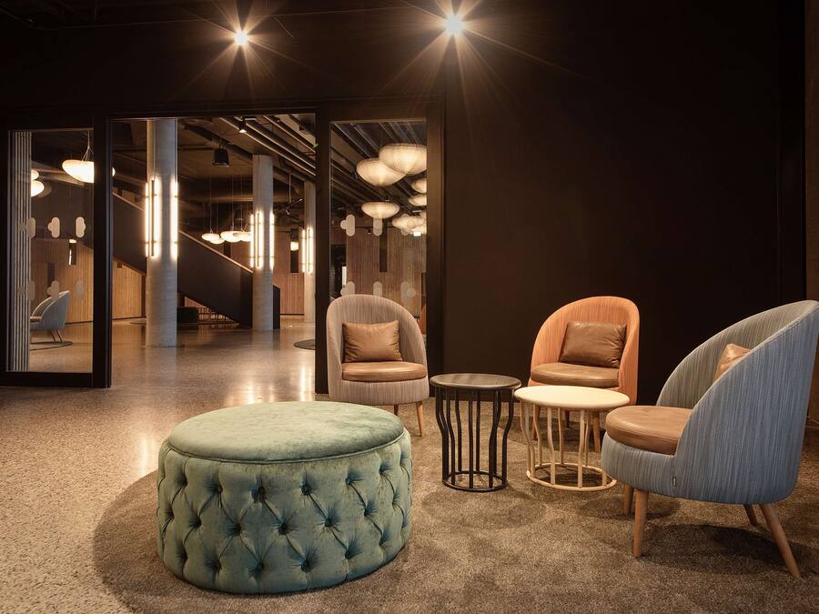 A modern lounge area with tufted ottoman, cushioned chairs, and pendant lighting.