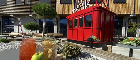 A modern building with a red structure, outdoor seating, and a variety of plants.